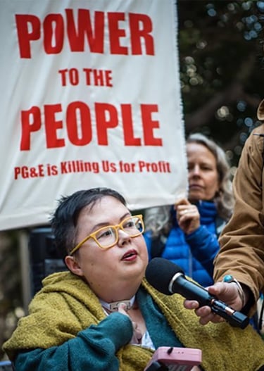Photo of Stacey at a protest with sign that reads "power to the people PG&E is killing us for profit"