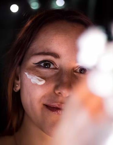 Woman smiling while applying face cream under her eye as part of a skincare routine.