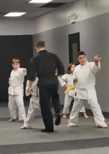 Children in white karate gi practice martial arts strikes during a youth training class.
