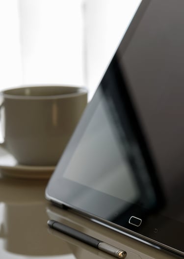 um-tablet-desligado-em-cima-de-uma-mesa-e-uma-xícara-de-café-ao-fundo