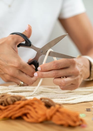 Una persona utilizando tijeras para cortar cuerda blanca de macramé sobre una mesa de madera.
