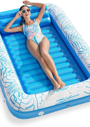 A woman relaxes on a blue inflatable tanning pool with tropical leaf patterns for summer backyard fun.