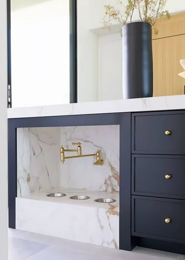 Elegant built-in cat feeding station with food bowls, marble-style wall, brass faucet and dark stora