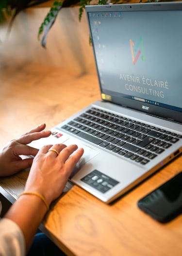 Mains d'un consultant sur un ordinateur portable avec le logo Avenir Éclairé Consulting 