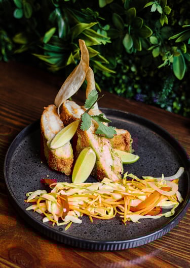 Crispy breaded shrimp appetizer served with fresh lime wedges and a side of vegetable slaw on a dark plate.