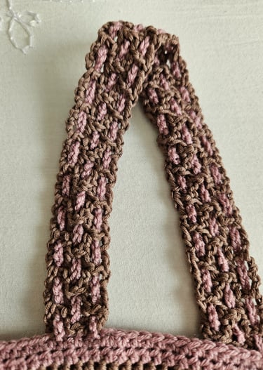 Close-up of a brown and pink crocheted shirt strap featuring a filet crochet pattern.
