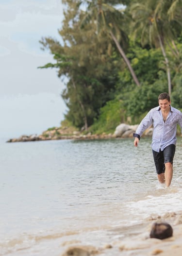 A happy couple holding hands and running along a tropical beach on Koh Samui, Thailand
