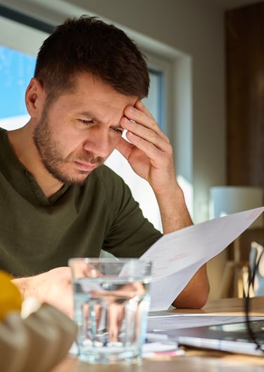 Stressed tradie reviewing business documents and bills at home with a laptop.