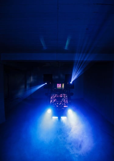 Professional event DJ setup with blue stage lighting and fog machine effects in a dark room.