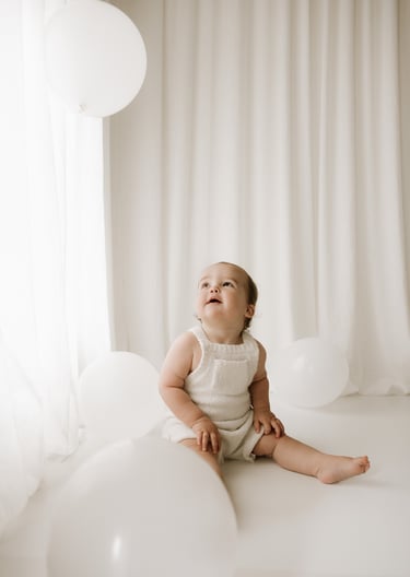 toddler looking up at white balloons in a cake smash session in Adelaide Hills studio