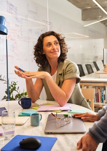 A smiling woman with curly hair participating in a collaborative office meeting at a round table.