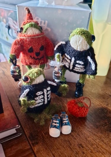 A group of knitted frogs sitting on a table in Halloween outfits