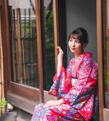 Woman in traditional floral kimono sitting in Japanese wooden doorway in Kyoto