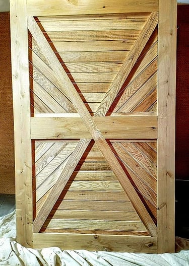 Handcrafted rustic sliding barn door made of light natural wood featuring a geometric X-brace design.