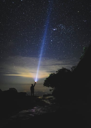 Eine Person richtet eine helle Taschenlampe in den dunklen Nachthimmel mit Sternen