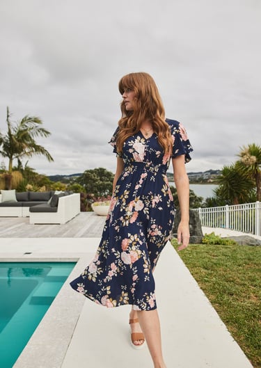 Fashion campaign photography - a woman in a floral dress standing on a patio by a pool