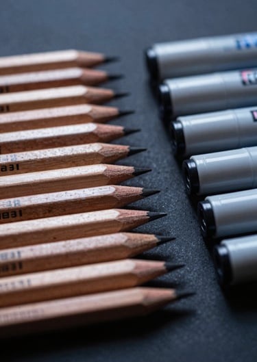 A macro photograph of professional drawing pencils and markers arranged neatly on a dark navy surface in a North American / US studio.