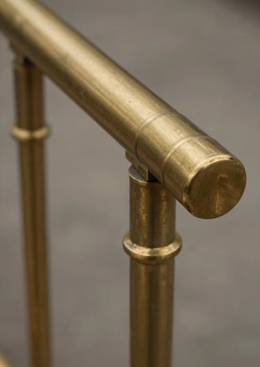 Close-up of a brass handrail ending. The metal has been turned and polished by hand, showing a warm bronze glow. Professional studio lighting, clean lines.