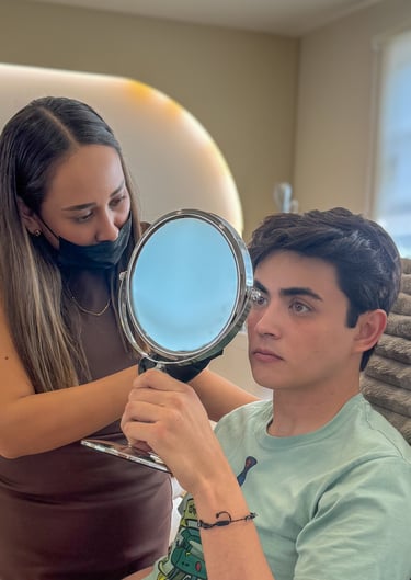 Esthetician showing a young male client his facial treatment results in a hand mirror.