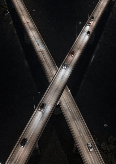 An aerial shot of a North American bridge at night, car headlights forming streaks of light. The composition is cinematic and expansive, using charcoal and off-white tones.