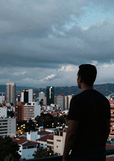 A silhouette of a man looking out over the Bogotá skyline at dusk, moody sky with hints of electric blue. Cinematic composition, South American / Colombian urban environment.