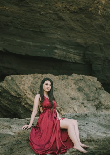 Intimate female portrait in red dress on the rocks during sunset at Pantai Nyanyi Bali.