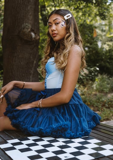 Portrait photo of a young Indonesian woman in a park with a chess table and whimsical blue dress