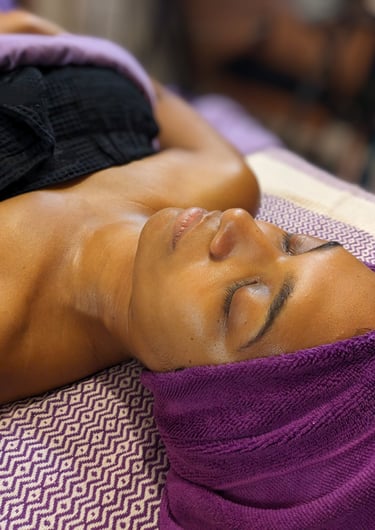 golden dark skin woman getting a facial at a spa with purple towels