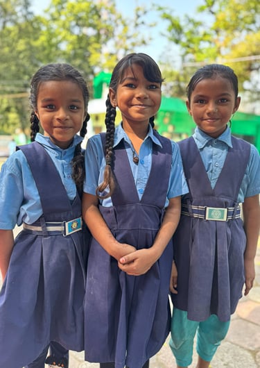 Three young schoolgirls in blue uniforms standing together smiling outdoors