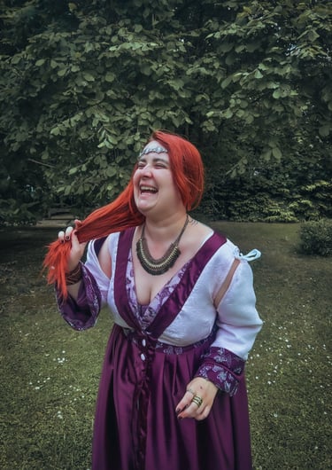 Femme rousse riante et joyeuse dans une robe violette et blanche dans un fond verdoyant