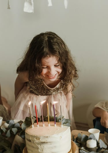 niña sonriente con cabello rizado mira las velas encendidas sobre un pastel de cumpleaños con betún