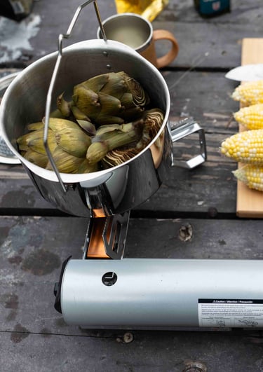 Artichokes cooking in a pot with corn of a cutting board