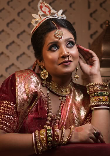 Bengali bride in red saree with bold kohl eyes, gold jewelry, chandan forehead design, and tradition