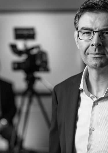 a man in a suit and glasses is standing in front of a camera