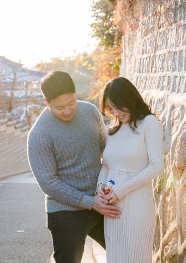 a pregnant woman and her husband are standing next to a stone wall
