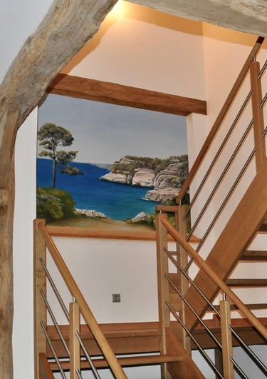 Une ouverture en trompe-l'oeil dans une cage d'escalier, invite au voyage en bord de mer. Le faux bois intègre l'ensemble.
