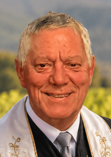 Portrait of a smiling senior wedding officiant wearing a formal stole outdoors.