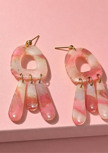 Pink and white marbled resin drop earrings with gold accents on a pink background.