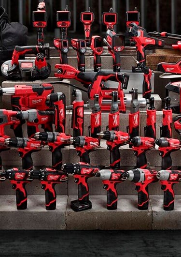 A wide assortment of red Milwaukee cordless power tools and heated gear displayed on concrete blocks.