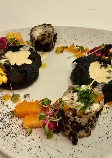 Gourmet plated fish with black squid ink puree, colorful cauliflower, and creamy sauce.