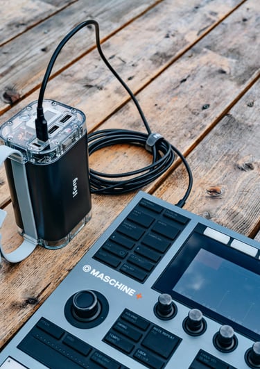 A professional music production setup featuring a Maschine+ controller and connected power source on a wooden table