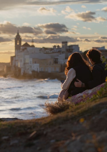 Couple watching a golden sunset over the Sitges coastline and Mediterranean Sea in Spain.