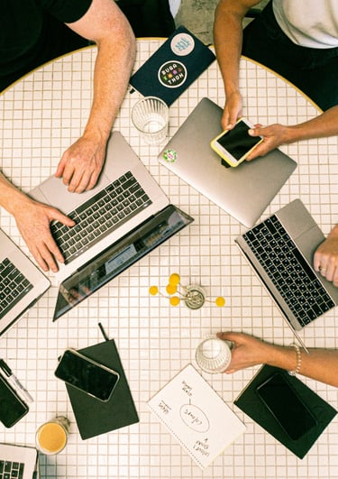 a group of people sitting around a table with laptops