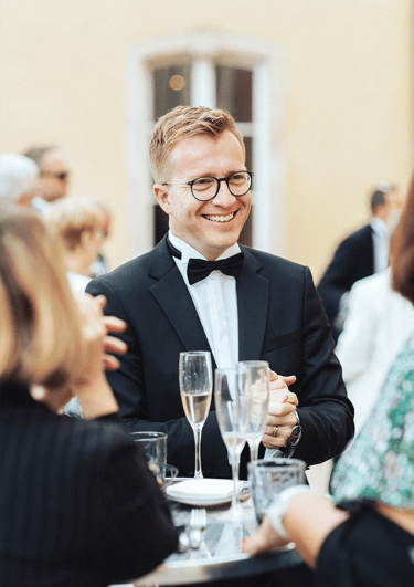 Marié élégant en costume souriant et discutant durant le vin d'honneur.
