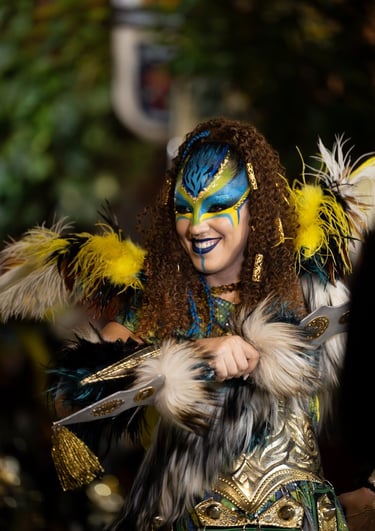 Smiling woman in fantasy warrior costume with blue face paint, feathers, and golden armor.