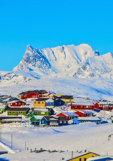 Colorful houses in a snow-covered Greenland village below a majestic arctic mountain peak.