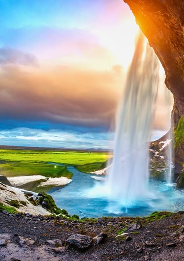 Seljalandsfoss waterfall in Iceland at sunset with water cascading into a blue pool and green meadows.