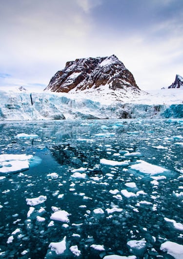 Melting glacier and floating sea ice in the Arctic ocean with snowy mountains under a cloudy sky.