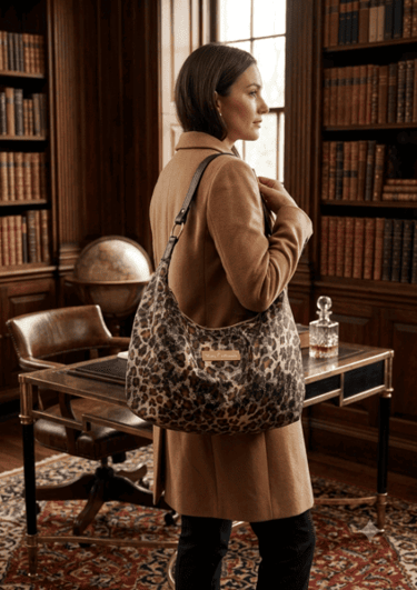 A woman in a tan coat carries a leopard print hobo shoulder bag in a classic library setting.