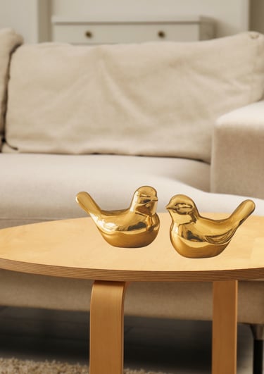 Par de passarinhos decorativos dourados em cerâmica sobre mesa de madeira em sala aconchegante.